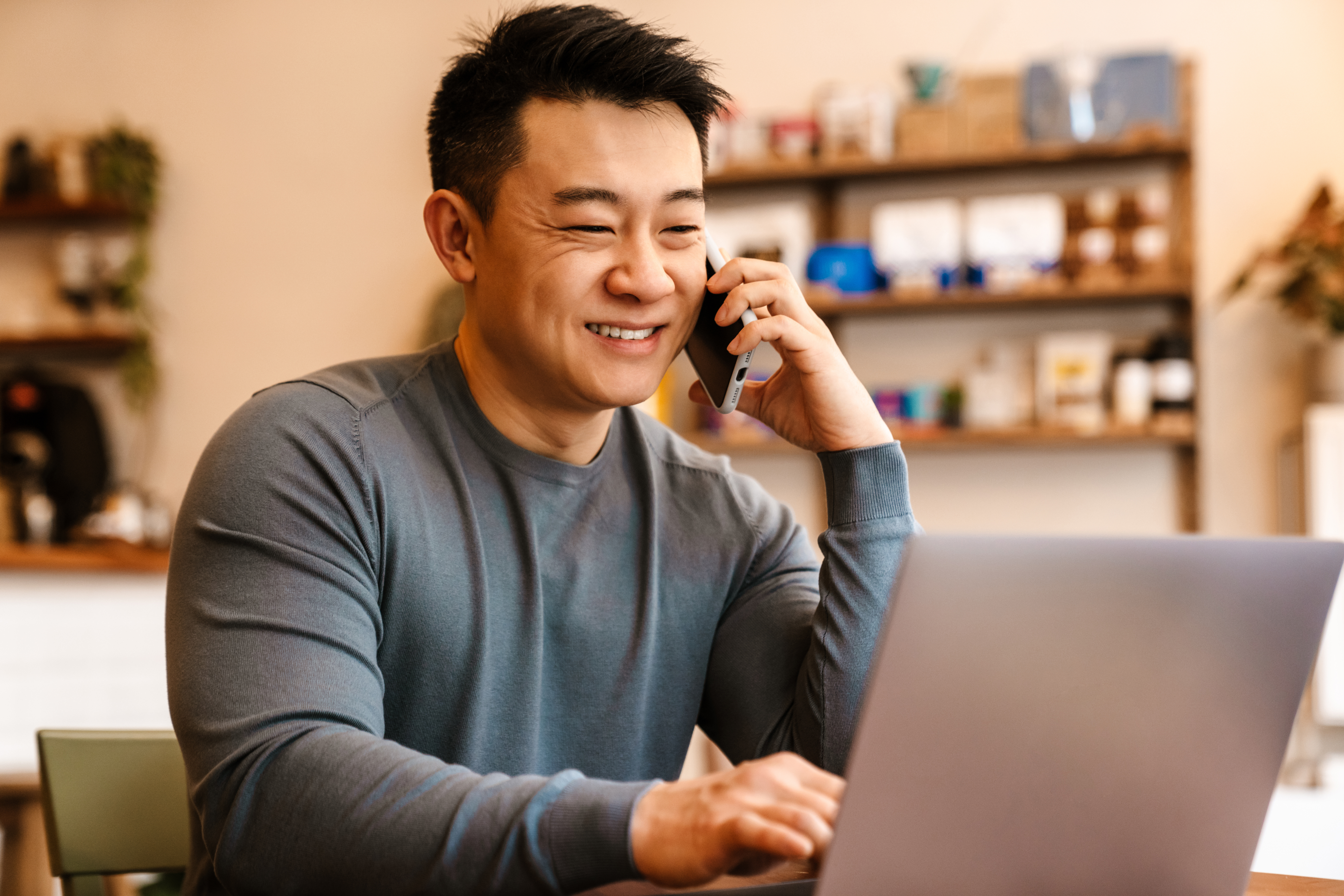 An aspiring investor talking on a mobile phone while looking at Funding's website on a laptop in a café